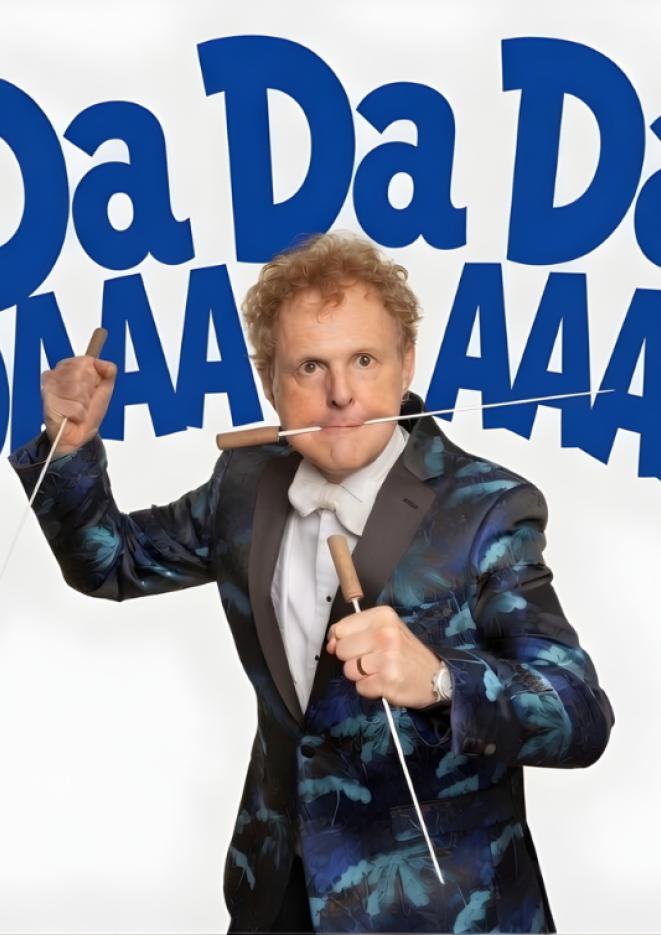 Musician Rainer Hersch stands in the centre of a white background wearing a black and blue tuxedo.