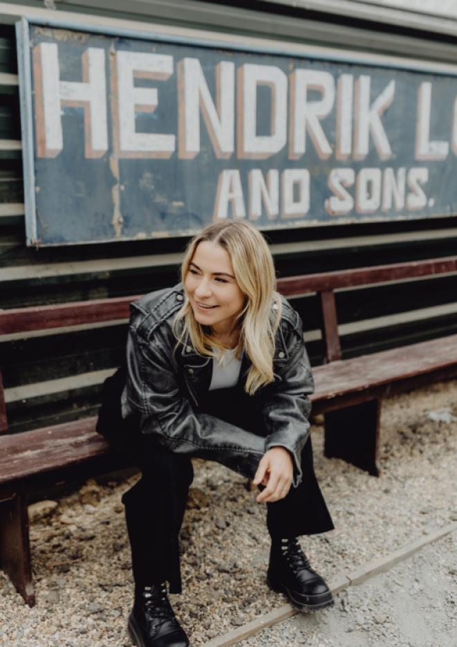 Musician Lucy Spraggan sits on a bench wearing an all black outfit.