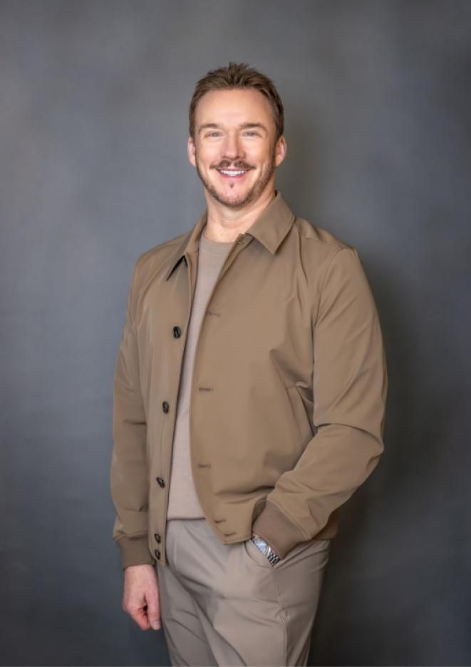 Singer Russell Watson stands against a grey background, wearing a smart beige outfit.