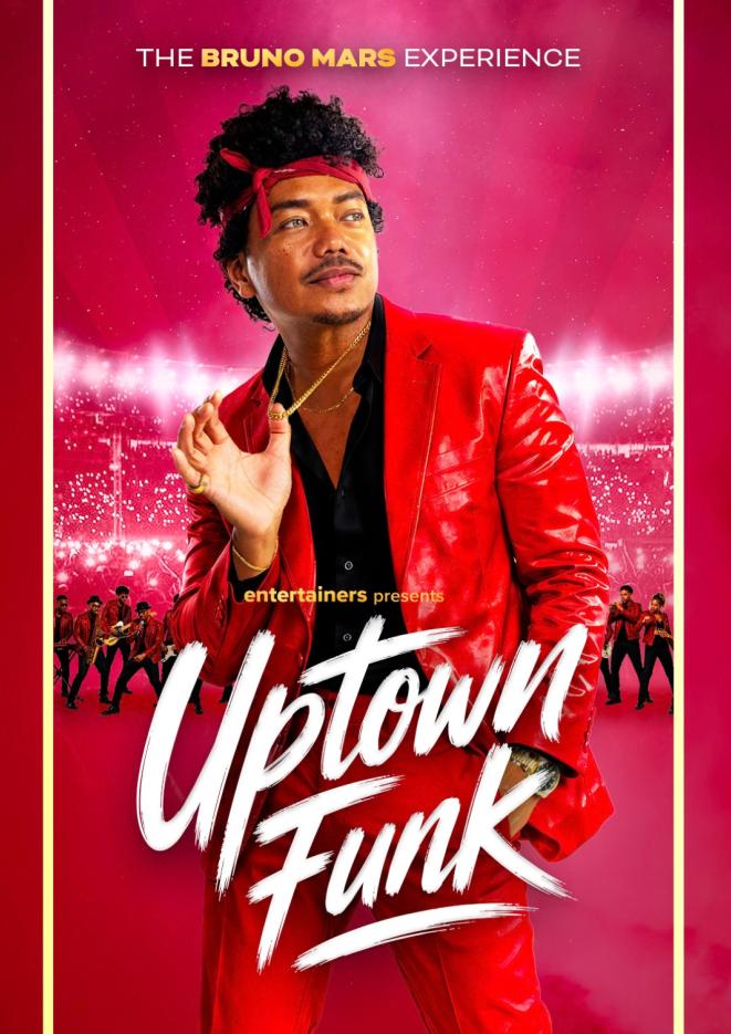 A man in a red shiny suit, red bandana and black shirt poses holding his gold necklace, against a red background with backup dancers.